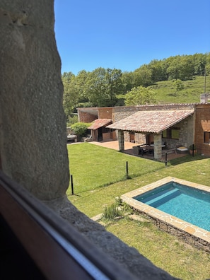 A view of a house with a swimming pool, stone walls, and a grassy yard.