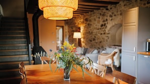 Una mesa de madera para comer con un jarrón de flores, un muro de piedra y una escalera al fondo.