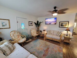 Una sala de estar con muebles de mimbre, televisión y ventilador de techo.