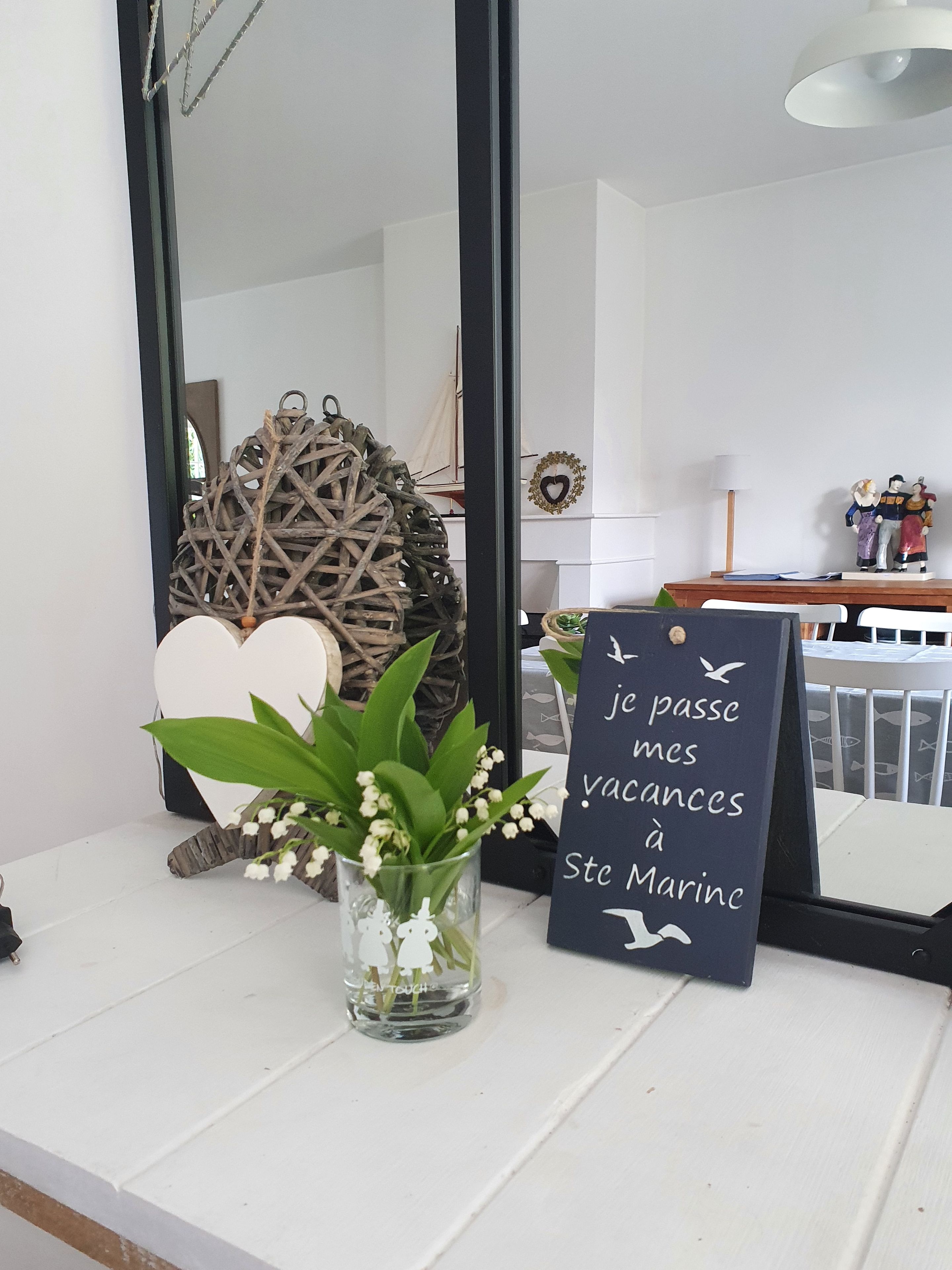 Una habitación con un espejo, un adorno en la pared, una planta pequeña en un florero de vidrio y un letrero con texto.