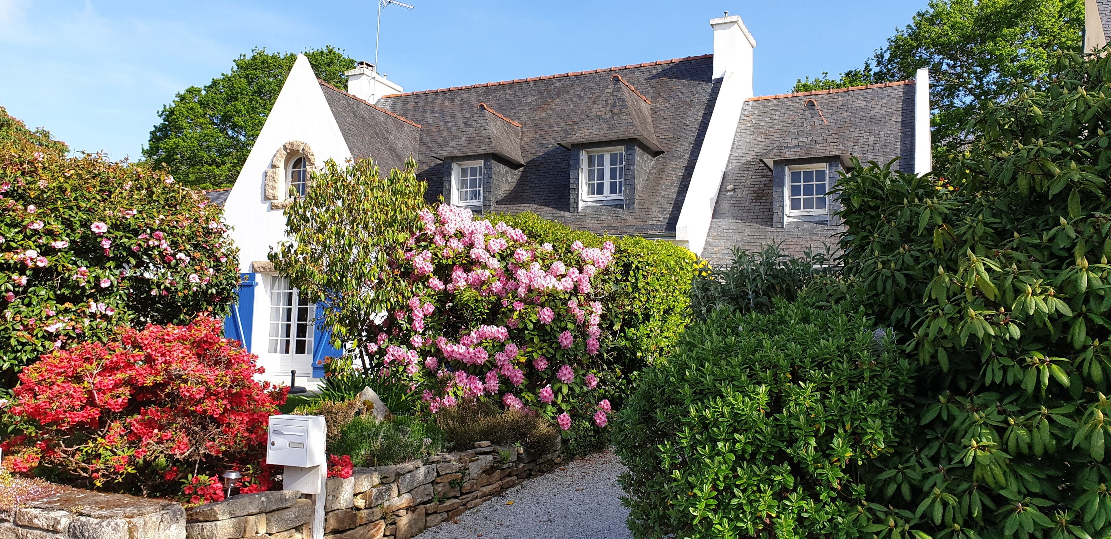 A traditional stone house with a steeply pitched roof, surrounded by lush gardens and flowering plants.