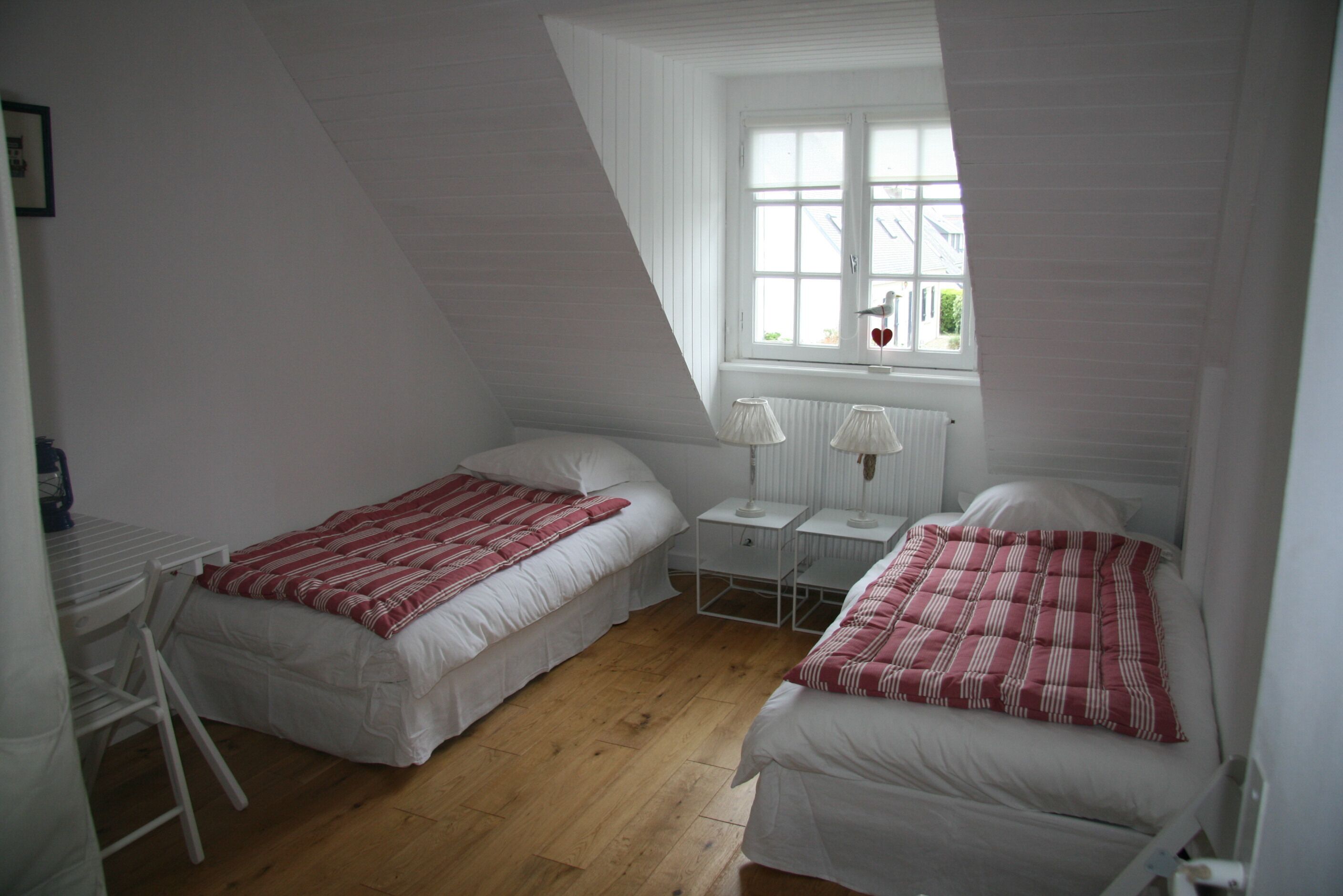 A small, white room with two beds, a window with a view, and a table.