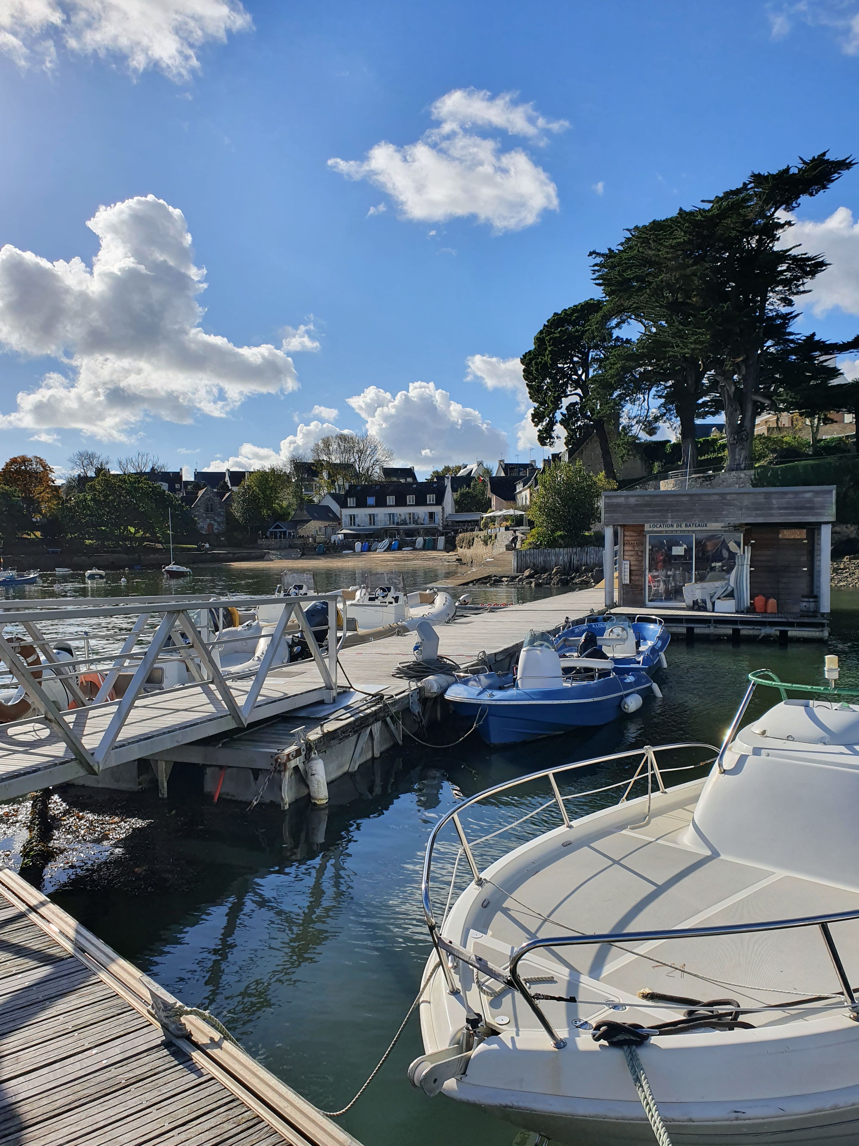 A marina with boats docked, a wooden pier, and a small building labeled 'LOCATION DE BATEAUX'.