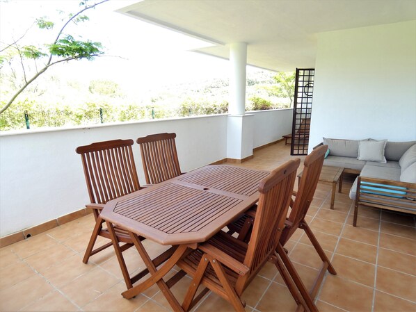 Un patio techado al aire libre con una mesa y sillas de madera, un sofá y vistas a zonas verdes.