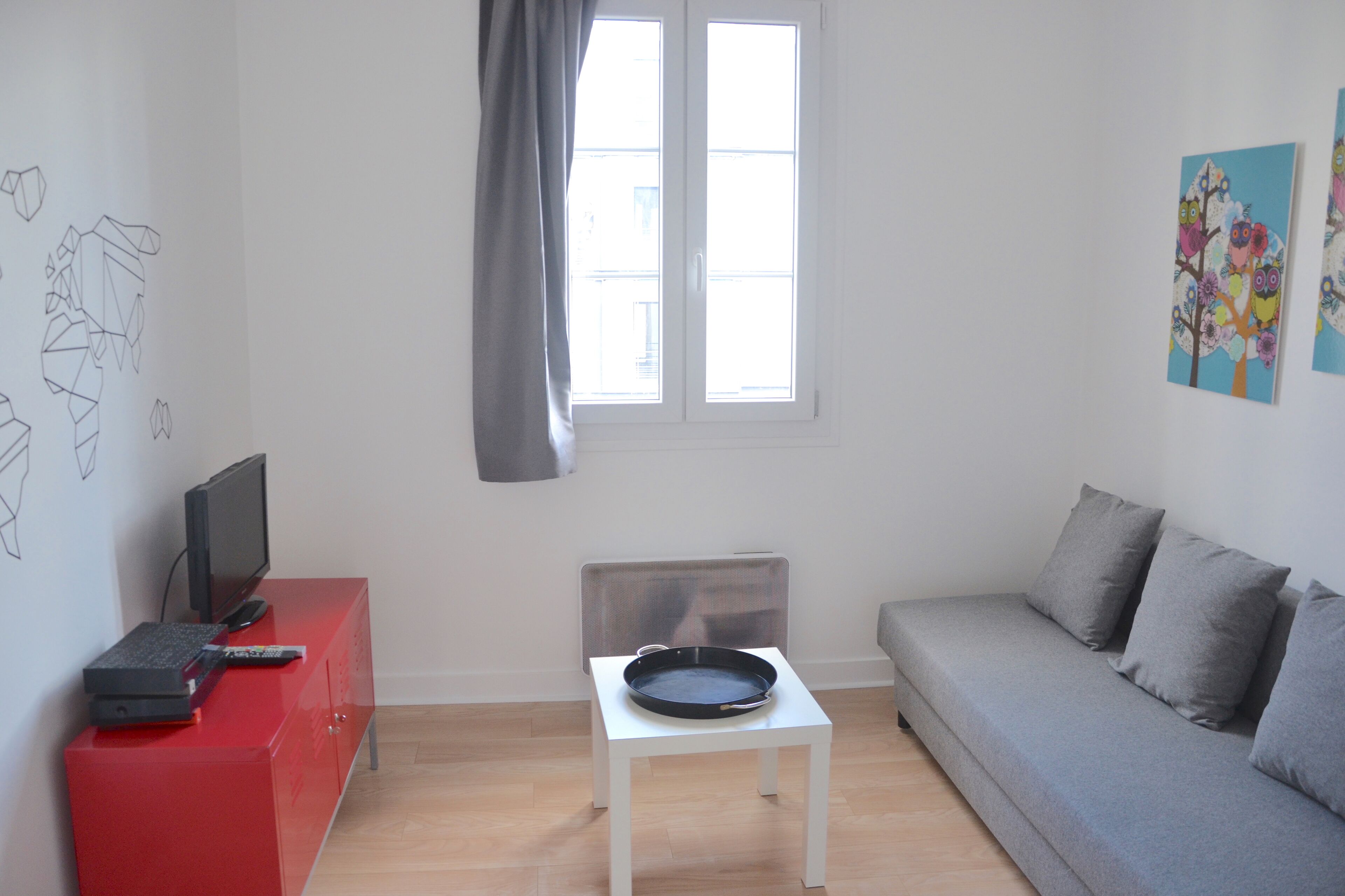 Un salon moderne avec un canapé gris, un meuble de télévision rouge, une table basse blanche et une fenêtre donnant sur un beau paysage.