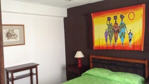 Un dormitorio con cama, mesita de noche, lámpara, un cuadro enmarcado y un tapiz colorido en la pared.
