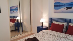 A bedroom with a bed, two nightstands, a mirror, and two wall-mounted paintings. - Apartment in residence (Altura)