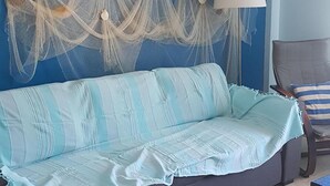 A living room with a dark sofa, a light blue striped throw, a macrame wall hanging, and a lamp. - Apartment in residence (Altura)