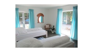 A bedroom with two beds, a chair, a plant, and a window with curtains. - Beltblick offers two large, comfortable apartments, located on Johannisberg (Fehmarn)