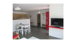 A modern kitchen with white cabinets, a dining table with chairs, a TV on a red stand, and pendant lighting. - Beltblick offers two large, comfortable apartments, located on Johannisberg (Fehmarn)