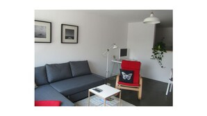 A modern living room with a grey sofa, a small white table, a red chair with a butterfly cushion, a floor lamp, and two framed pictures on the wall. - Beltblick offers two large, comfortable apartments, located on Johannisberg (Fehmarn)