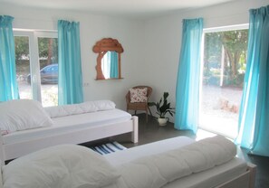 Un dormitorio con dos camas, una silla, una planta y una ventana con cortinas.