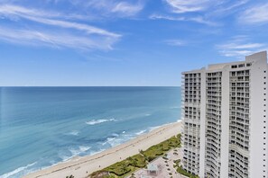 Um hotel moderno com vista para a praia, com varandas, piscina no terraço e um jardim bem cuidado.