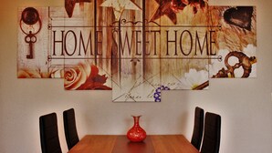 Une table à manger avec quatre chaises, un vase rouge et une œuvre d’art murale portant l’inscription « HOME SWEET HOME ».