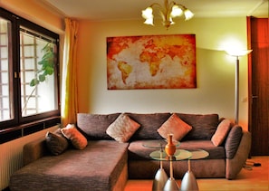 Uma sala de estar com sofá seccional, mesa de centro de vidro e um quadro de um mapa-múndi na parede.