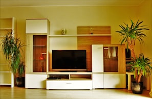 Uma sala de estar moderna com televisão de tela plana, estantes de madeira e plantas em vasos.