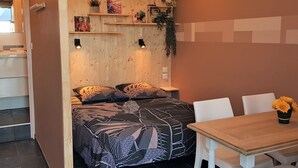 Un dormitorio con cama, mesitas de noche, cabecero de madera, una pequeña mesa con sillas y una ventana.