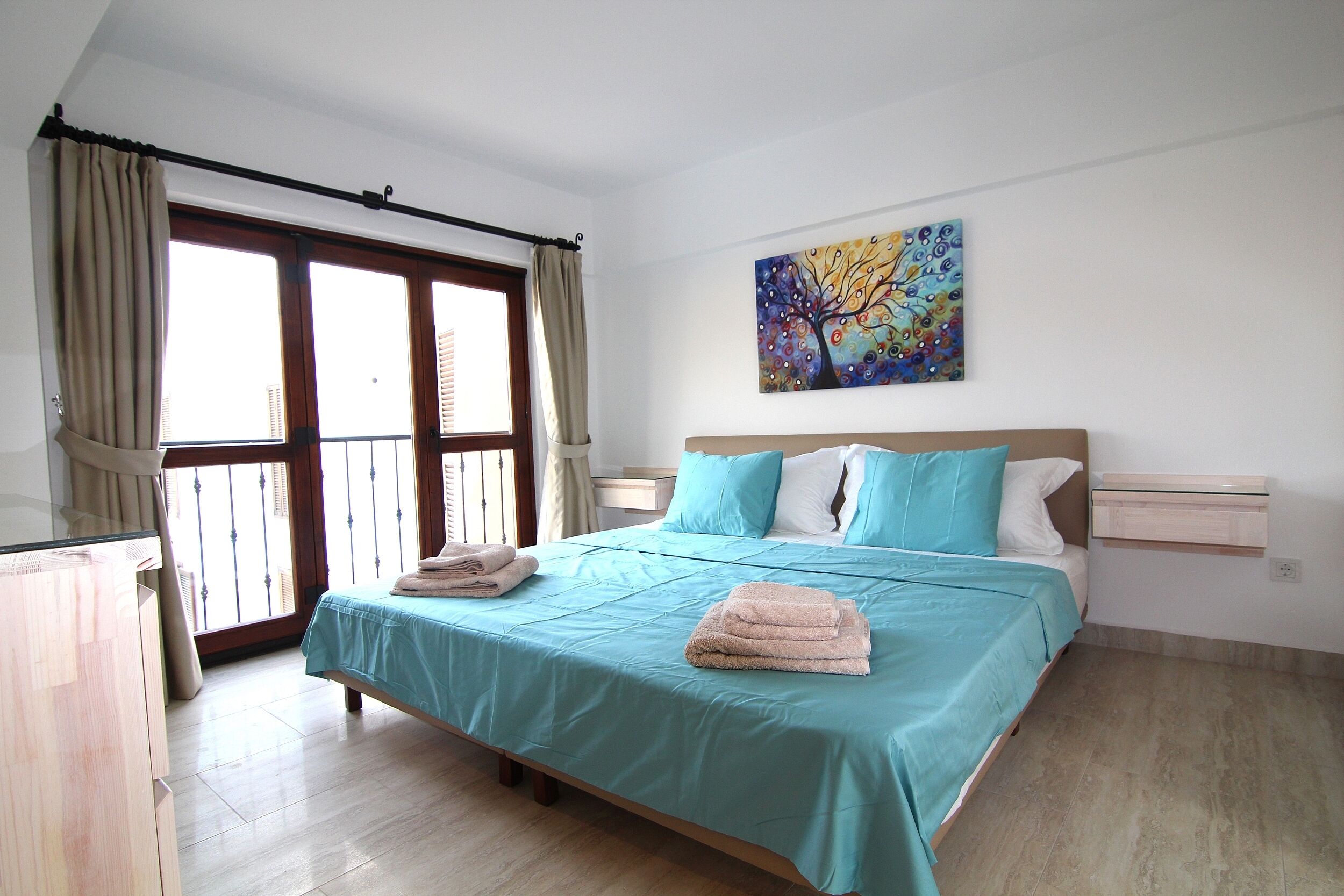 Un dormitorio con cama, cortinas, un cuadro y una ventana.