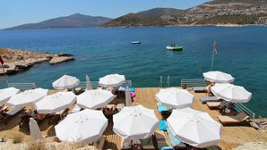 A wooden deck with white umbrellas and lounge chairs overlooking a calm sea with boats. - Town Centre Penthouse Apartment With Two Sea View Private Roof Terraces (Kalkan)