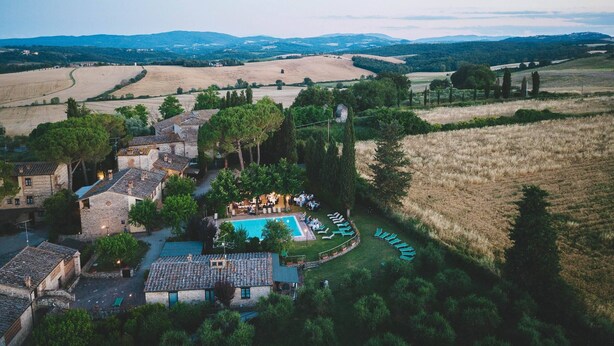 Eine Vogelperspektive zeigt ein ländliches Anwesen mit Pool, Liegestühlen und traditionellen Steingebäuden, umgeben von Feldern und Bäumen.
