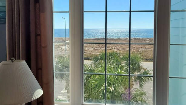 Habitació amb finestra gran que ofereix vistes a la platja i palmeres.
