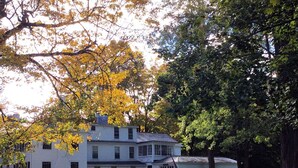 A two-story white house with a front porch and a garage. - Miner Cottage-Historic Antique Home just steps from the Equinox Resort (Manchester)