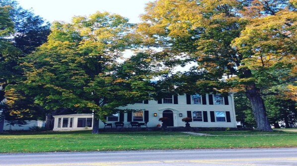 Une maison à deux étages avec un porche, entourée d’arbres aux feuilles d’automne.