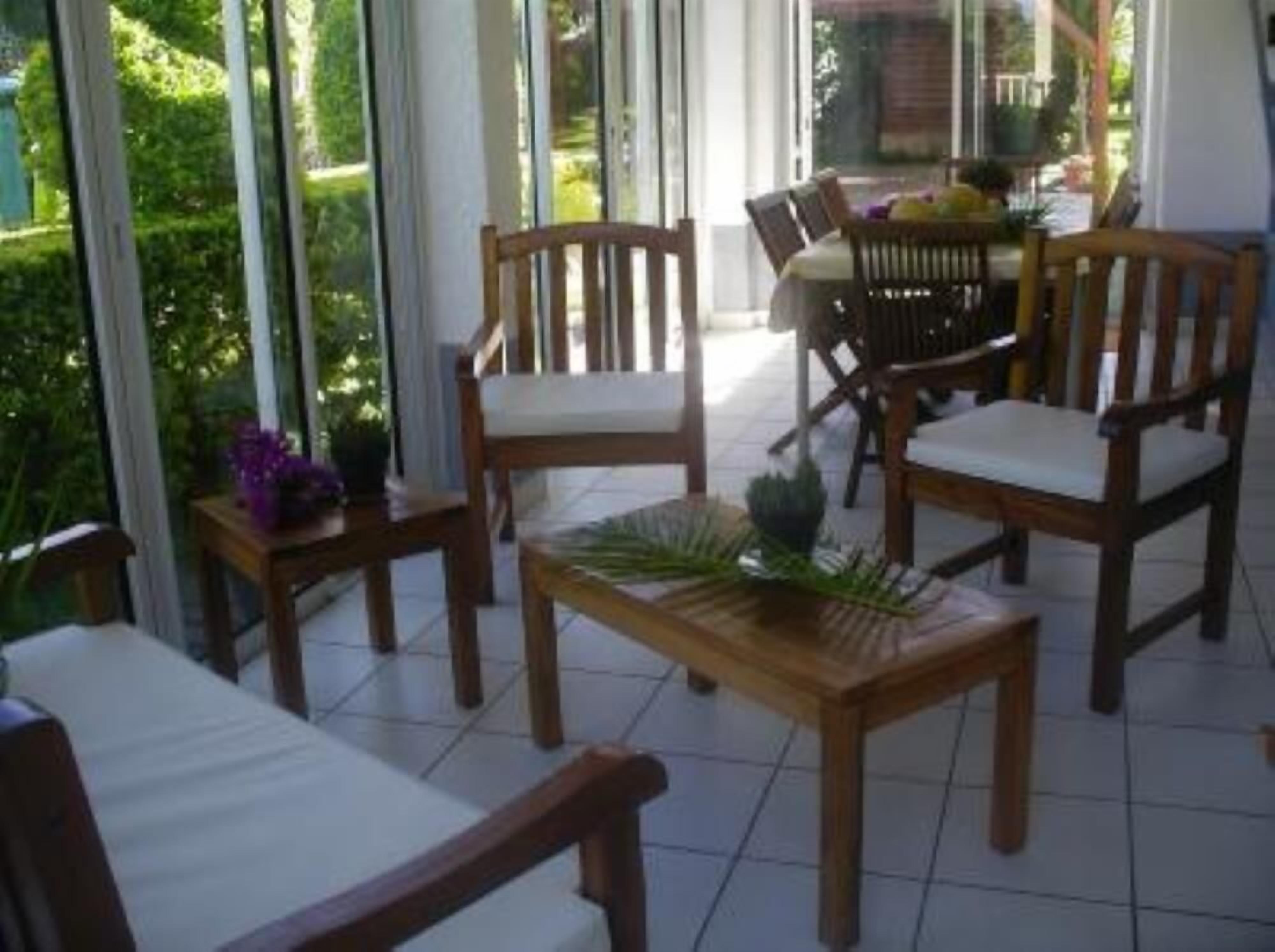 Un patio iluminado por el sol con mobiliario de madera y vistas a un jardín.
