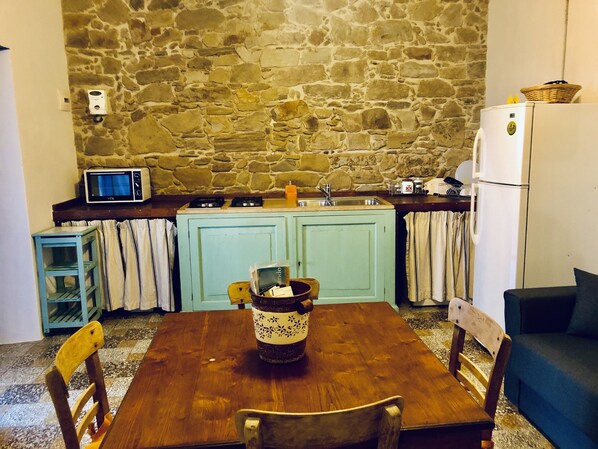 A kitchen with a stone wall, a microwave, a sink, and a refrigerator.