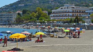 A beach with people sunbathing and swimming, umbrellas, and a building with statues in the background. - Old fisherman's house overlooking the sea, along the Capo d'Orlando promenade (Capo D'orlando)