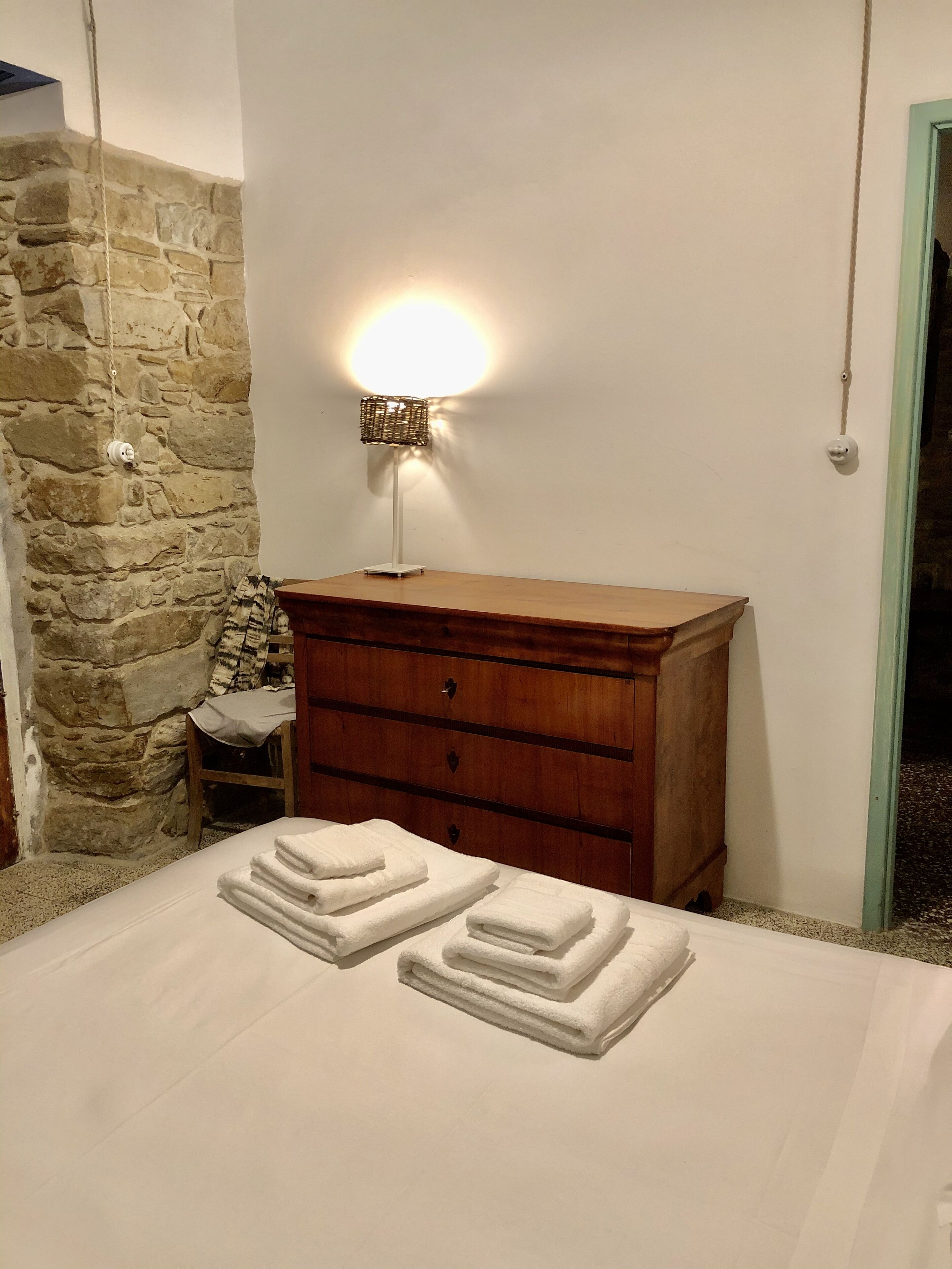 Un dormitorio con una cama, un aparador de madera, una pared de piedra y una lámpara de pared.