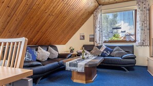 Un salon chaleureux avec un plafond en pente, un ensemble de canapés, une table basse et une vue sur la verdure à l’extérieur.