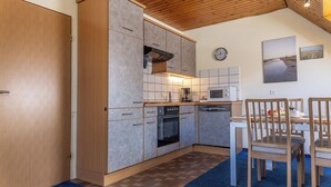 Une cuisine compacte équipée d’un four à micro-ondes, d’une cuisinière et de placards, un coin repas avec des chaises et une horloge au mur.