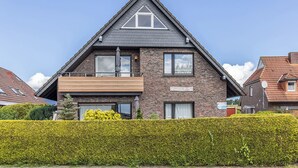 Une maison à deux étages, dotée d’un toit triangulaire imposant, d’un balcon et d’une haie bien entretenue à l’avant.