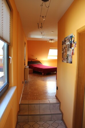 Un pasillo estrecho con piso de madera, una cama roja a lo lejos y una pared con un collage de fotografías.