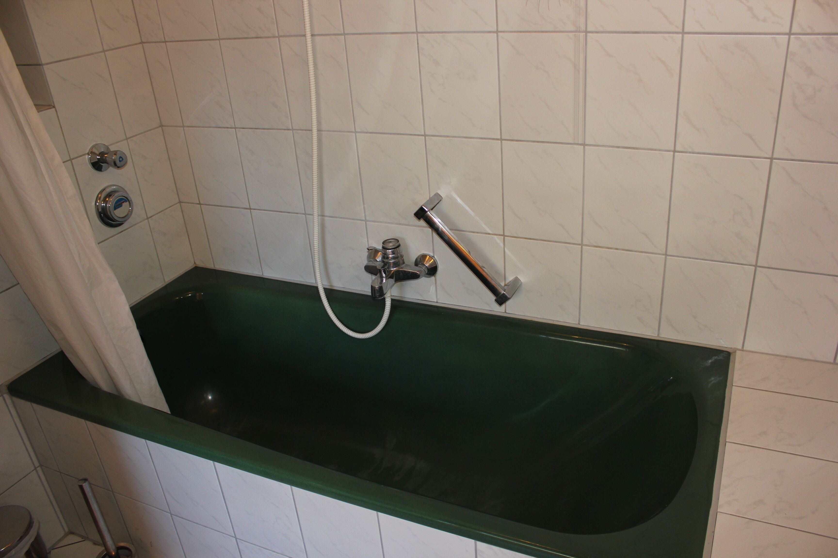 A bathroom with a green bathtub, white tiled walls, and a showerhead.