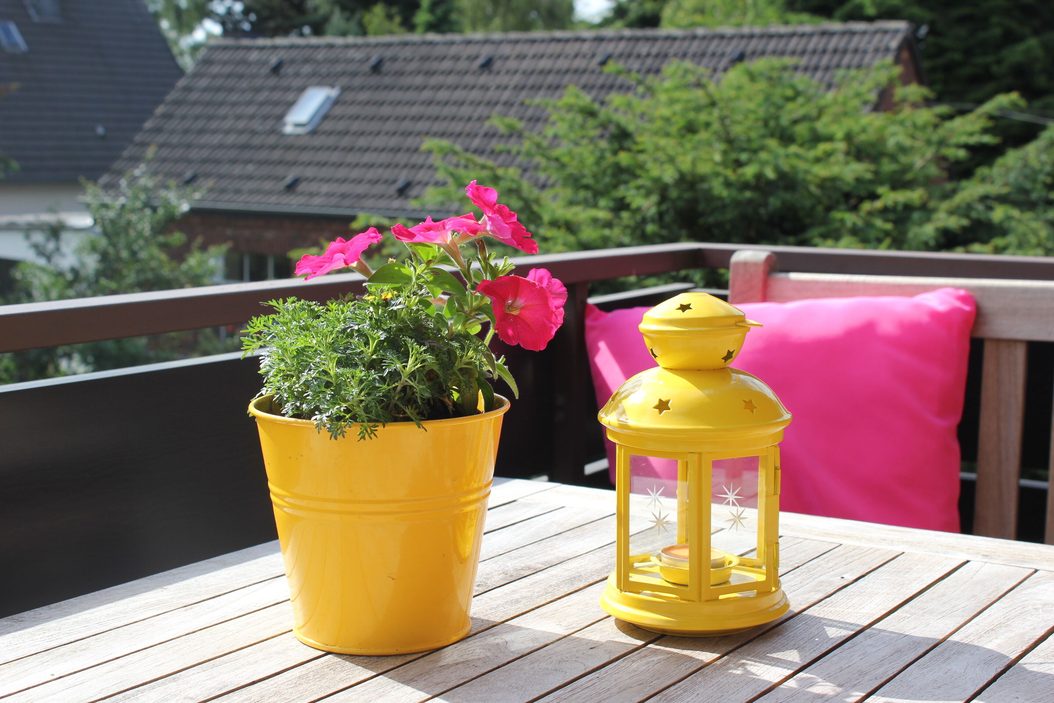 Um deck de madeira com um vaso amarelo de flores e um lampião amarelo.