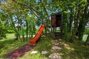 Un parque infantil con un tobogán y una casita de madera rodeada de árboles.