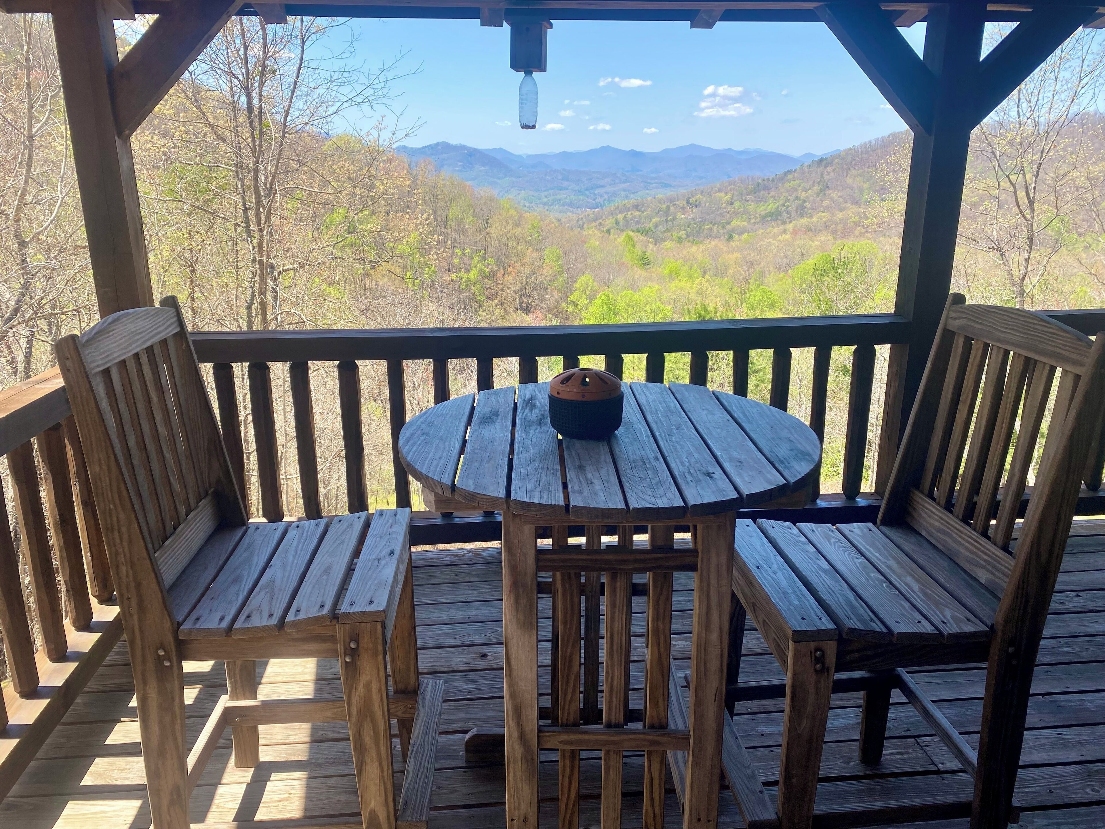 Un terrazzo in legno con un tavolo rotondo e due sedie, con vista su un paesaggio montuoso.