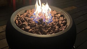 En bålplads med flammer, omgivet af sten, på en træterrasse.