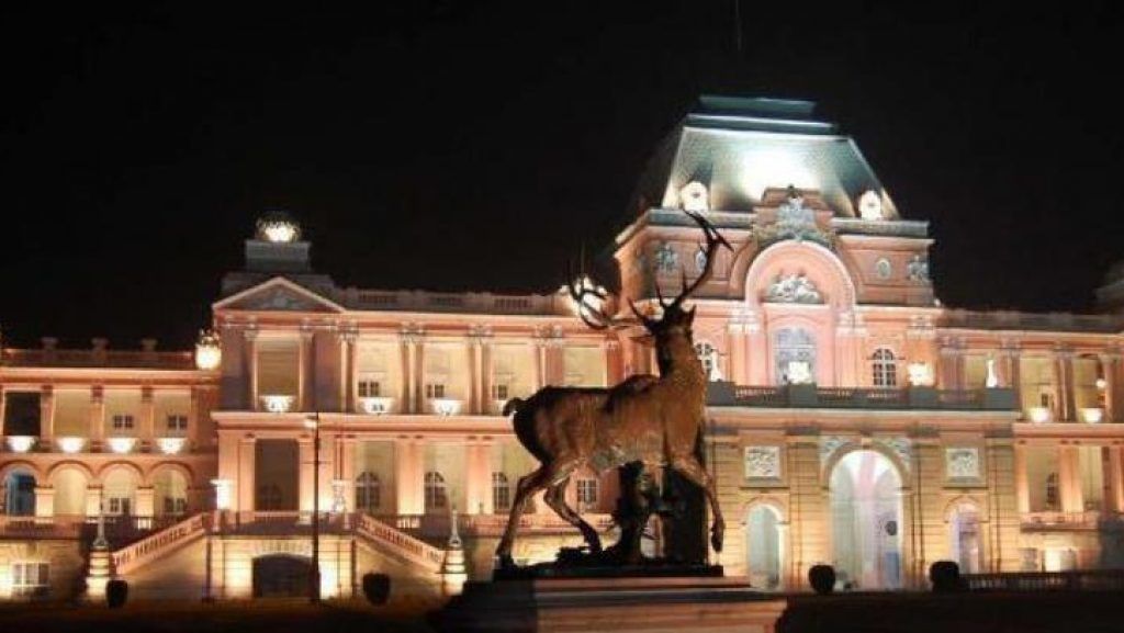 Un edificio grande de arquitectura clásica, una estatua de un ciervo y una fachada bien iluminada.