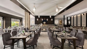 Um restaurante moderno com piso de mármore, cadeiras estofadas em cinza e iluminação pendente.