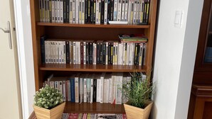 En træreol med flere hylder fyldt med bøger, to krukker med planter og dekorative genstande.