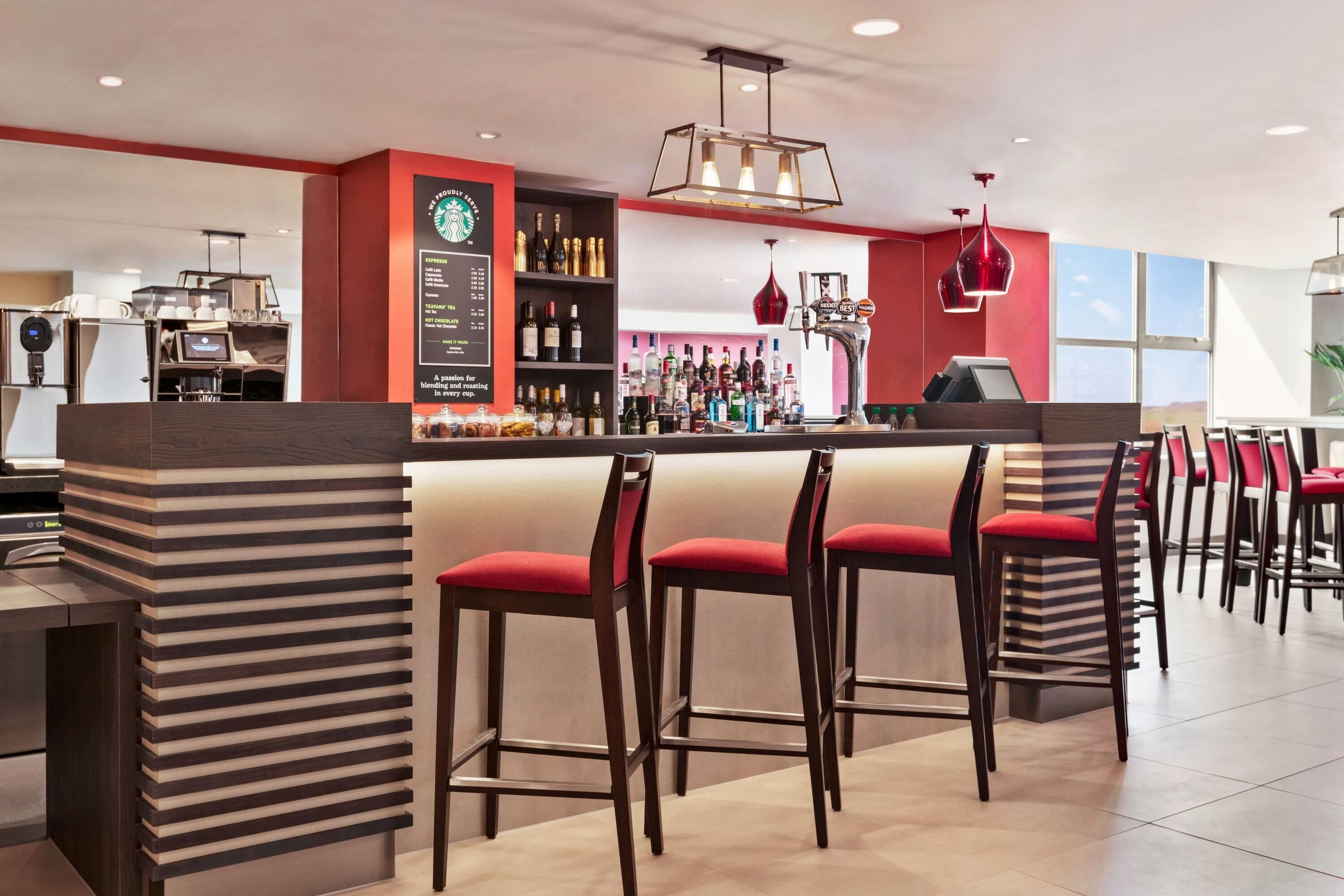A modern bar area with a red and beige color scheme, bar stools, and a variety of liquor bottles.