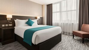 Hotellihuone, jossa on suuri sänky, yöpöytä, tuoli ja ikkuna, jossa on ohuet verhot.