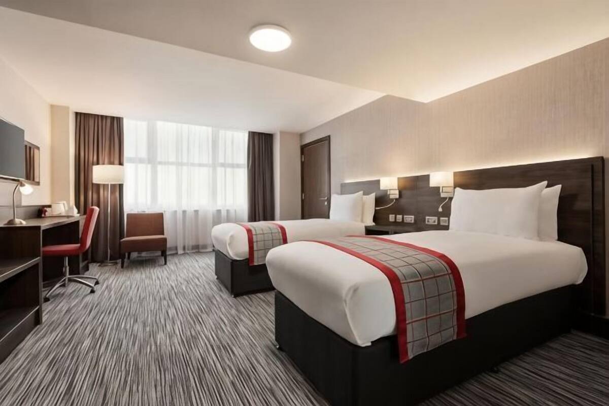 Habitación de hotel con dos camas, un escritorio, una silla y un televisor.