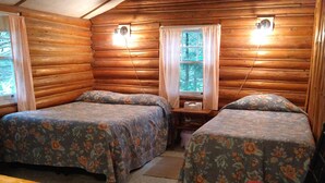 A log cabin room with two beds, a small table, and a chair. - Rustic log cottage, River-view, Pet-friendly, Downeast Maine (Edmunds Township)