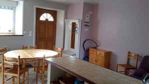 A dining area with a round wooden table and chairs, a wooden cabinet, and a vacuum cleaner. - Apartment with large garden prox. from the sea and landing beaches (Étréham)