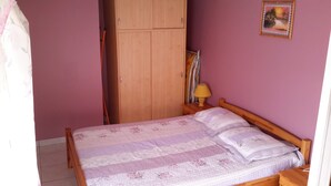 A bedroom with a bed, wooden wardrobe, and a nightstand with a lamp. - Apartment with large garden prox. from the sea and landing beaches (Étréham)