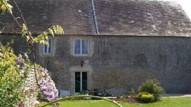 A stone building with a sloped roof, a central entrance, and a small garden area with a hose and plants. - Apartment with large garden prox. from the sea and landing beaches (Étréham)